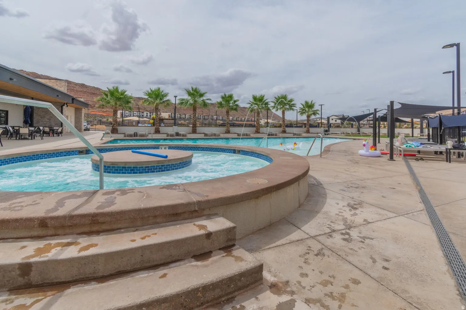 Resort-style pool area featuring a circular hot tub with blue tile accents, a large swimming pool, and a concrete deck