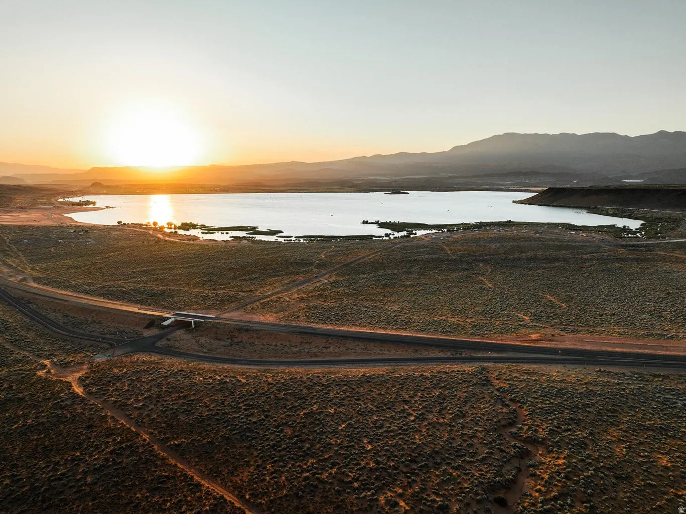 Expansive aerial landscape featuring a large lake, surrounding desert terrain, and distant mountains
