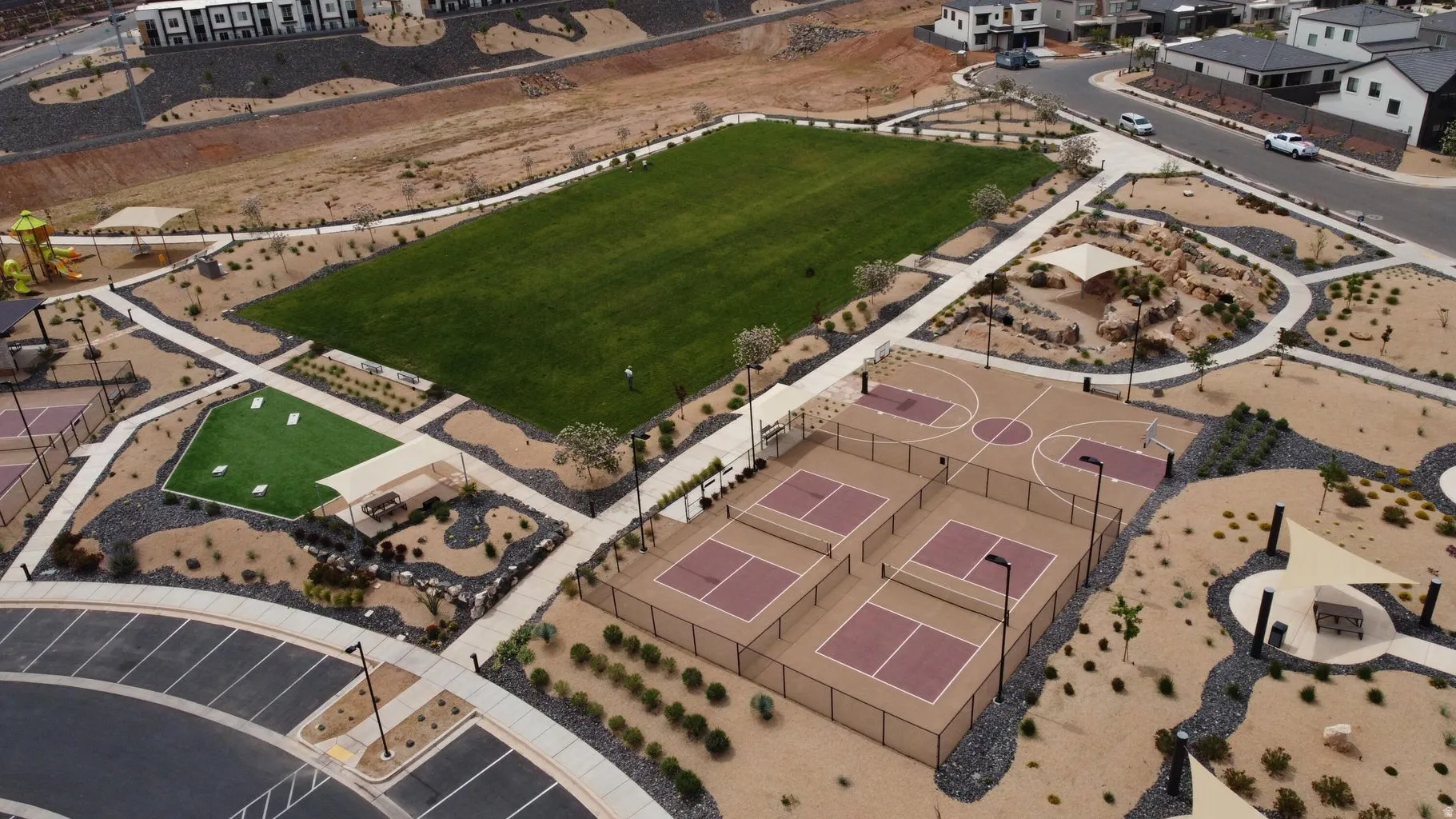 Community park with a large manicured lawn, basketball court, multiple pickleball courts, and playground