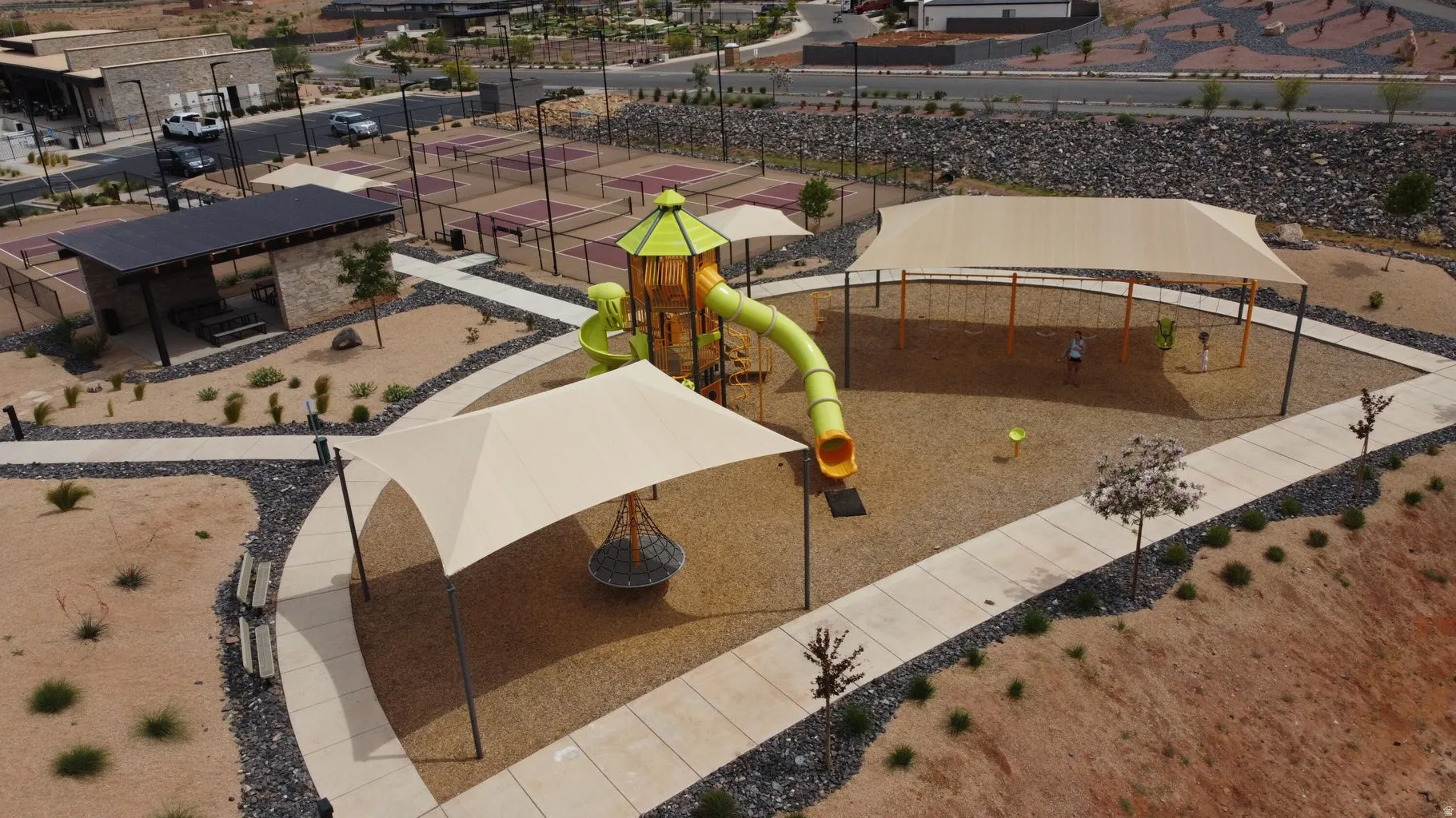 Community playground featuring a multi-level play structure with slide, multiple shade structures, and a dedicated swing set area