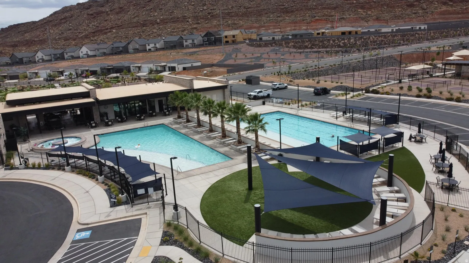 Community pool and spa area featuring a modern recreational building, multiple shaded seating areas, and surrounding hardscape