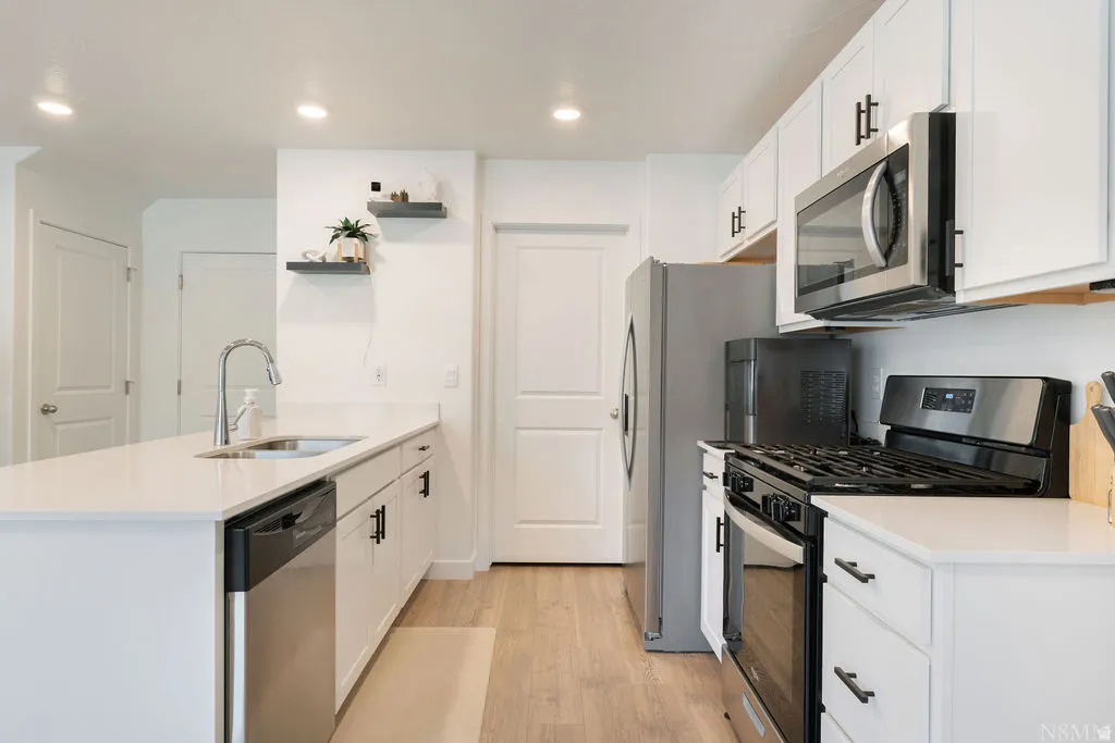 Modern kitchen featuring white cabinetry, light-colored countertops, stainless steel appliances, and wood-finish flooring