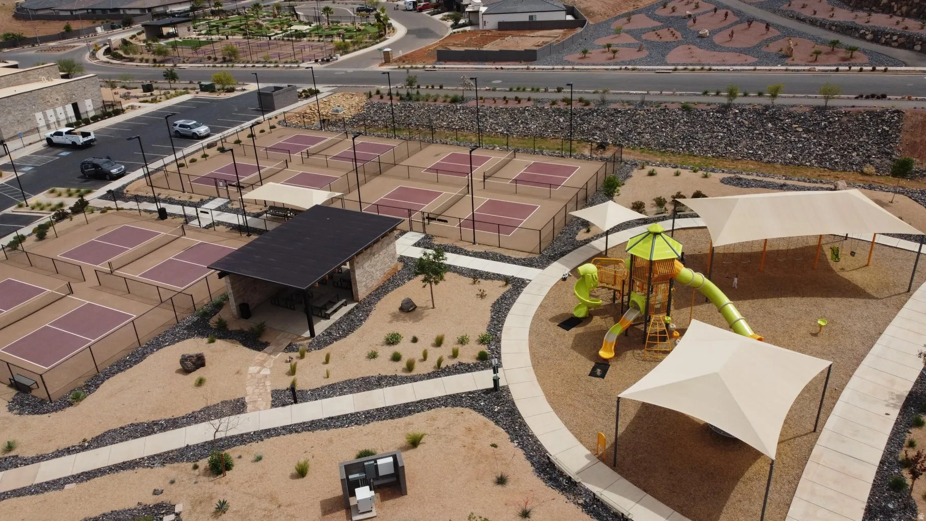 Community recreational area featuring multiple pickleball courts, a covered pavilion, a playground with slides and swings, and shade structures