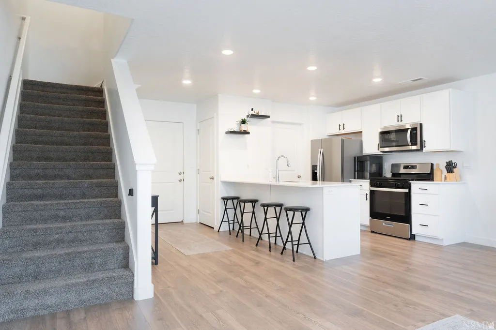 Open-concept living area featuring wood-finish flooring, recessed lighting, and a carpeted staircase