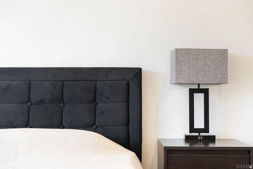 Tufted headboard with a dark fabric finish, accompanied by a modern bedside lamp with a rectangular shade, set on a dark wood-finish nightstand