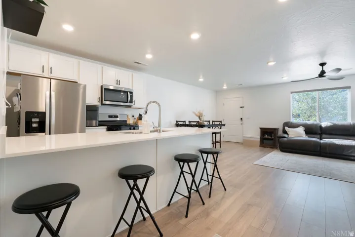 Open-concept kitchen and living area featuring white cabinetry, stainless steel appliances, a kitchen island with seating, recessed lighting, and wood-finish flooring
