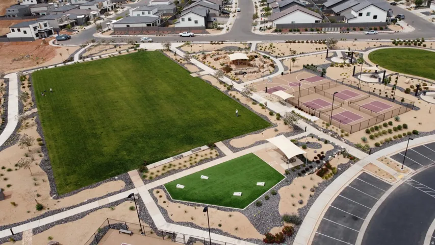 Community recreation area featuring a large manicured lawn, multiple sports courts, artificial turf play areas, shaded seating, and integrated walking paths