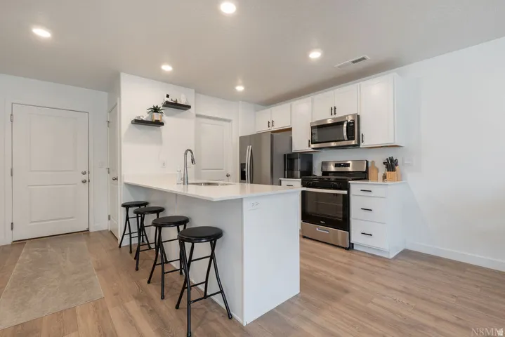 Modern kitchen featuring white cabinetry, stainless steel appliances, a center island with sink, recessed lighting, and wood-finish flooring