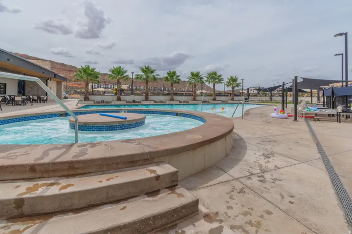 Resort-style pool area featuring a circular hot tub with blue tile accents, a large swimming pool, and a concrete deck