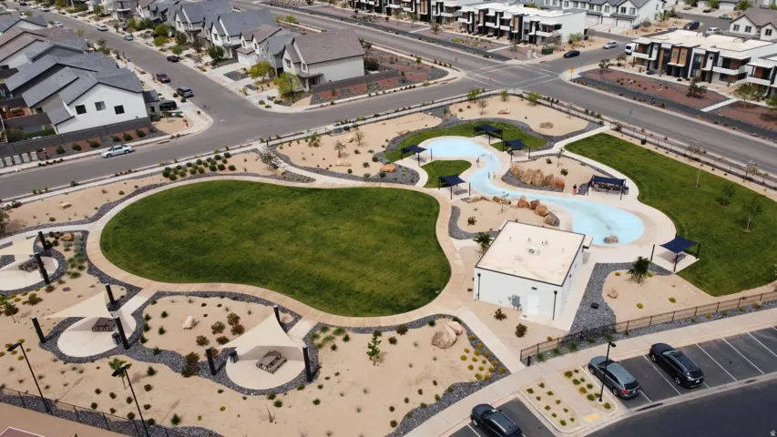 Expansive community park featuring a large green space, winding pool, shade structures, and surrounding desert landscaping