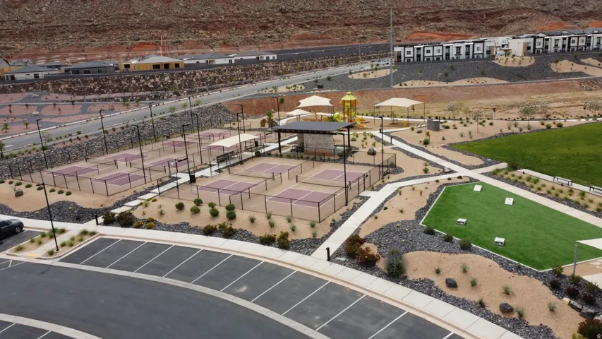 Community amenity area featuring multiple pickleball courts, a central shaded pavilion, a children's play structure with shade canopies, an artificial turf recreation area, and extensive hardscaping with desert landscaping