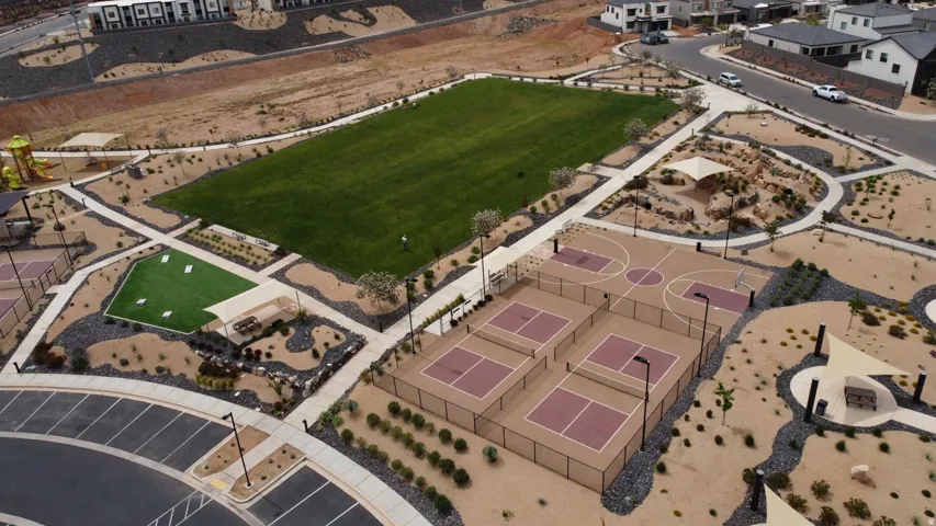 Community park with a large manicured lawn, basketball court, multiple pickleball courts, and playground