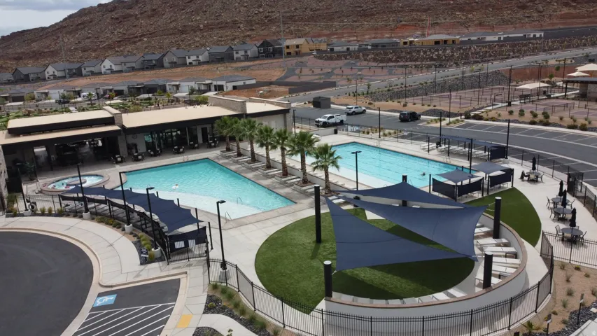 Community pool and spa area featuring a modern recreational building, multiple shaded seating areas, and surrounding hardscape