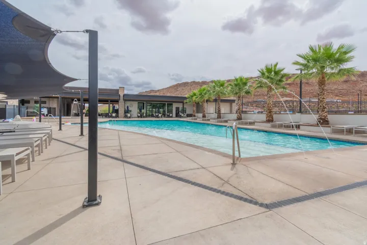 Resort-style pool area featuring a large swimming pool with water features, a surrounding concrete deck, and shaded lounge seating