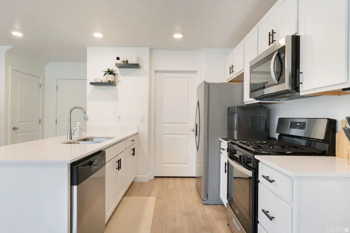 Modern kitchen featuring white cabinetry, light-colored countertops, stainless steel appliances, and wood-finish flooring