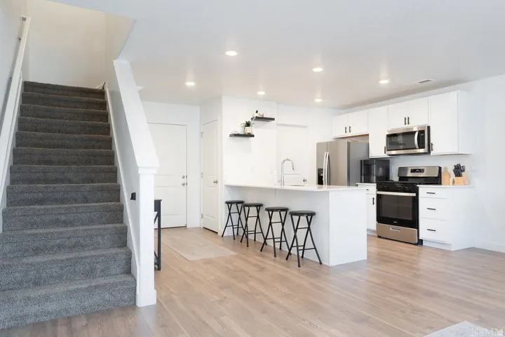 Open-concept living area featuring wood-finish flooring, recessed lighting, and a carpeted staircase