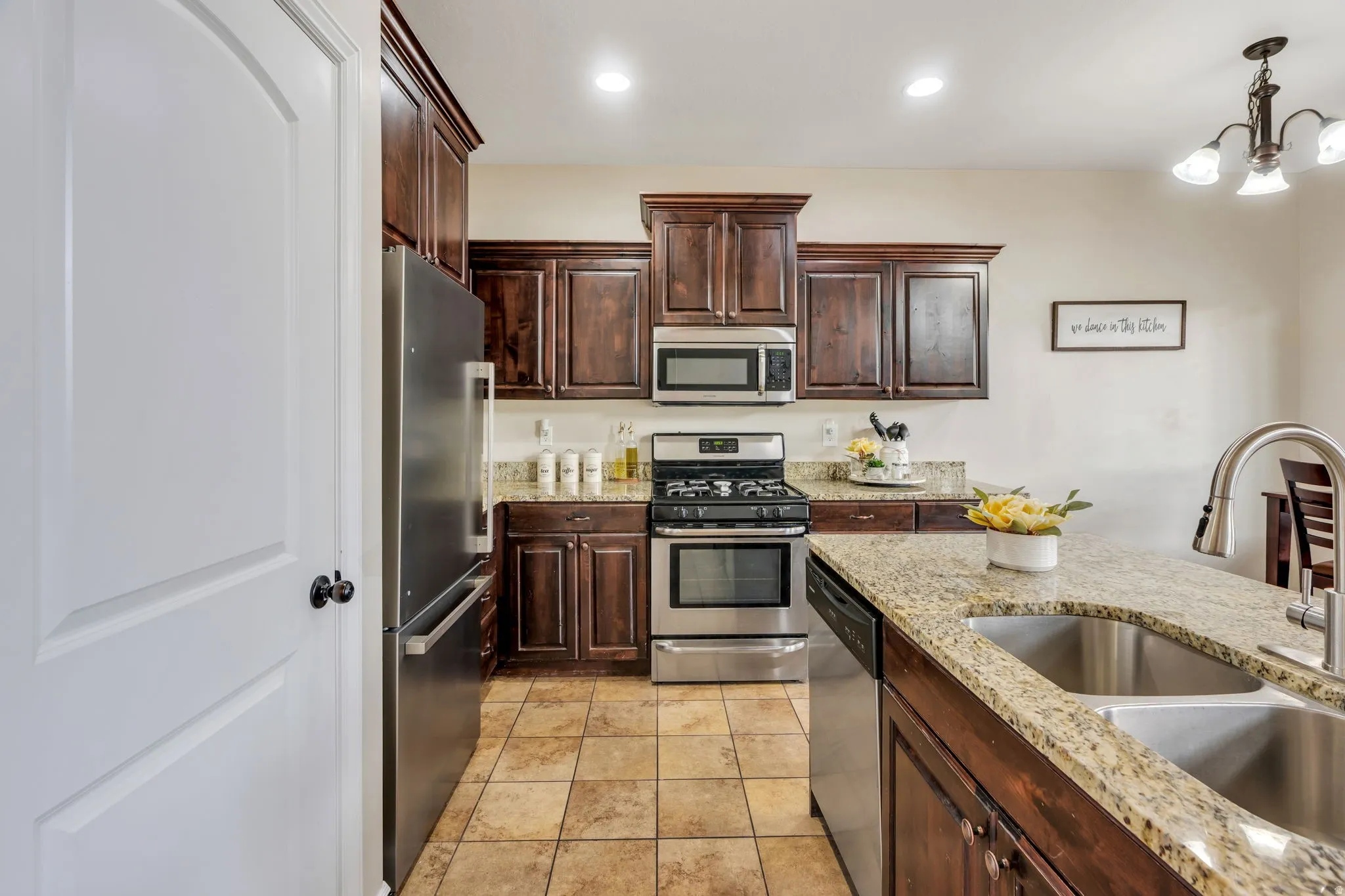 Kitchen featuring wood-finish cabinetry, stainless steel appliances, granite countertops, and tile flooring