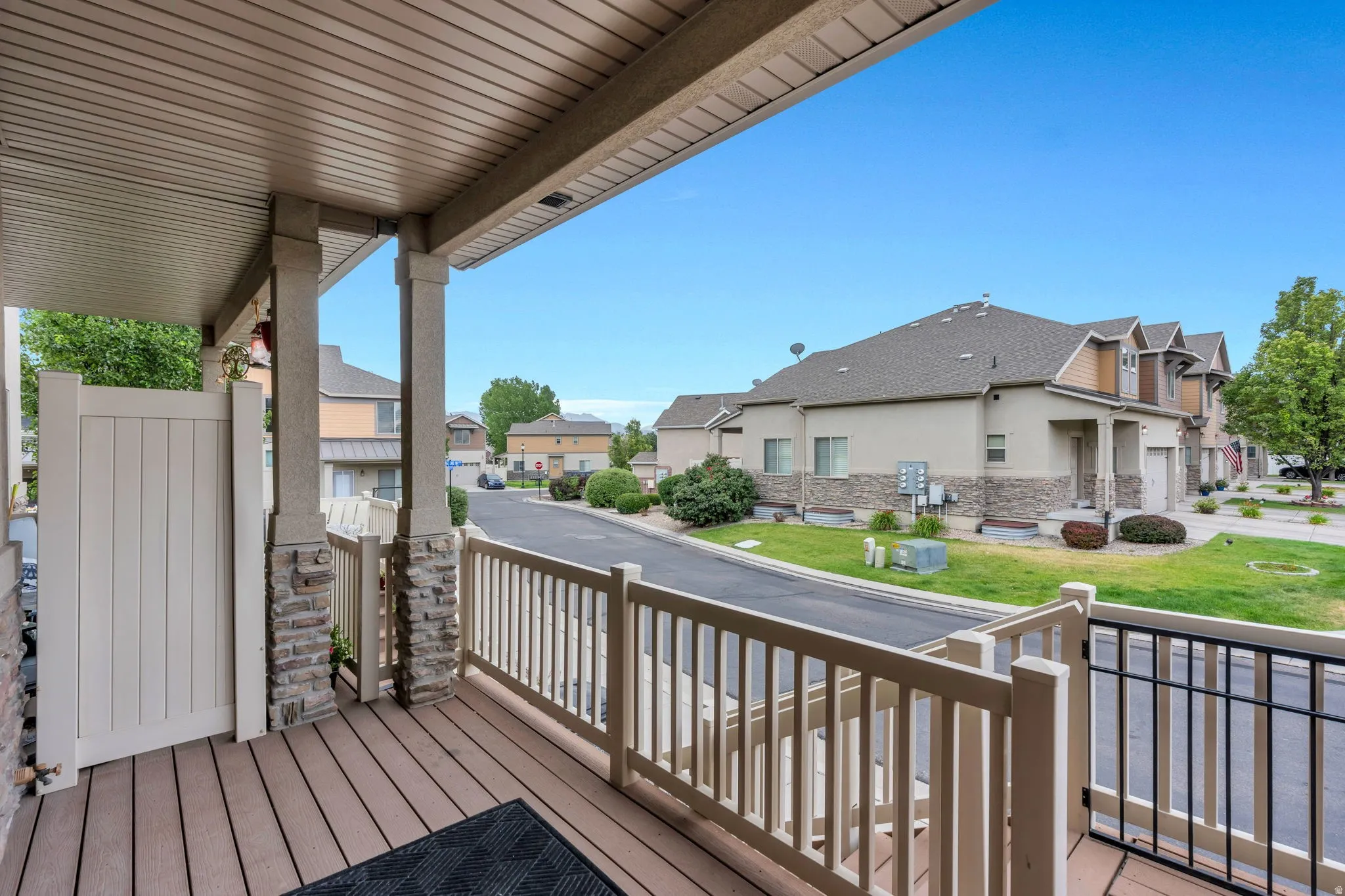 Covered front porch featuring composite wood-finish decking, white railings, and stone-clad support columns