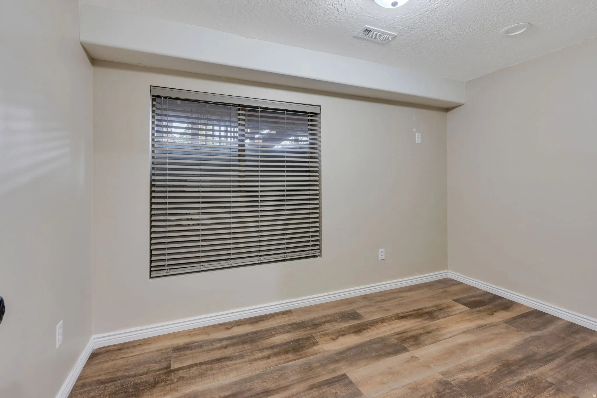 Room featuring a horizontal window with blinds, wood-finish flooring, light-toned wall paint, and white baseboards