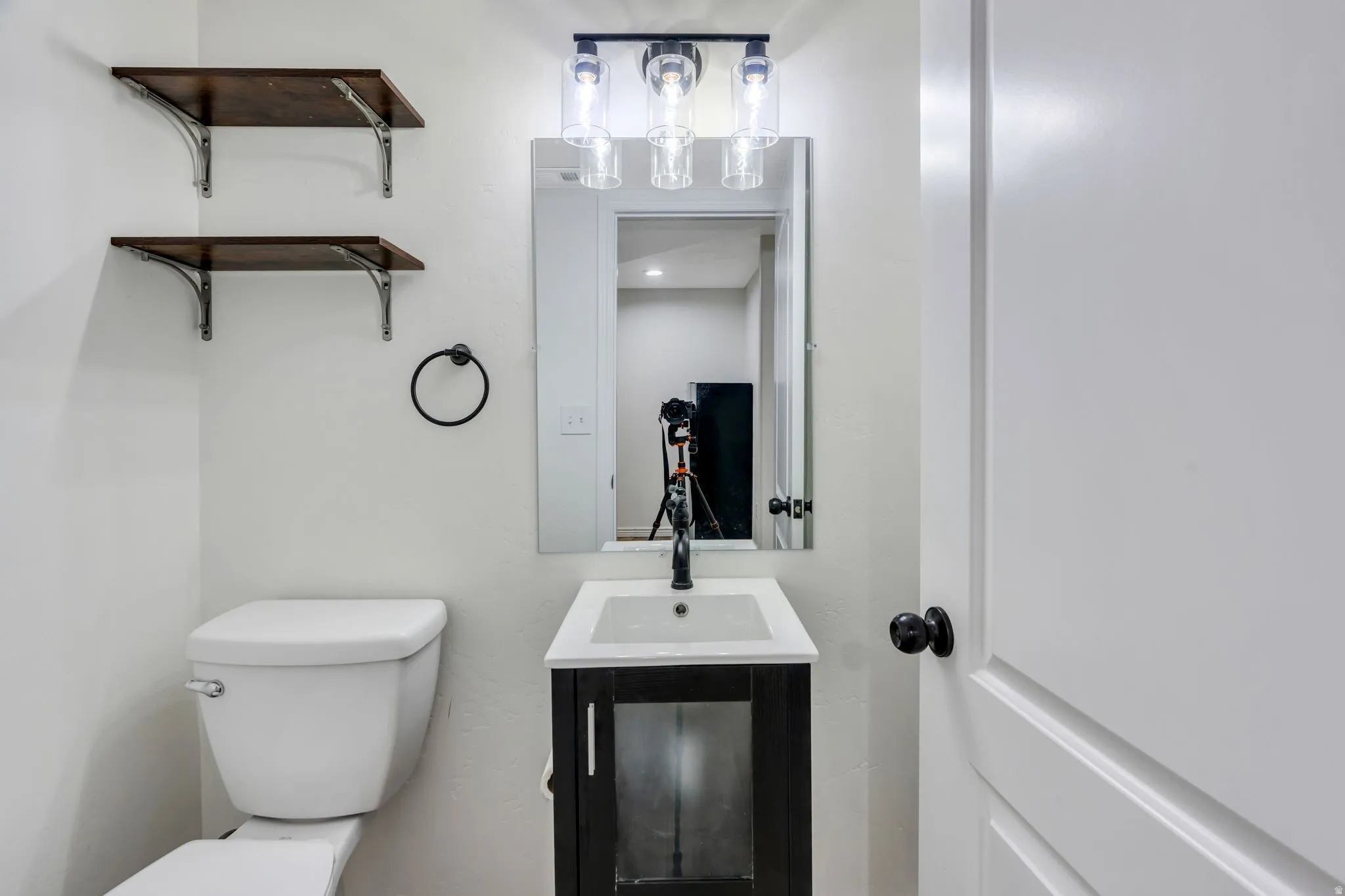 Bathroom featuring a dark wood-finish vanity with a white countertop and rectangular sink, complemented by a wall-mounted mirror and a three-light fixture with clear glass shades