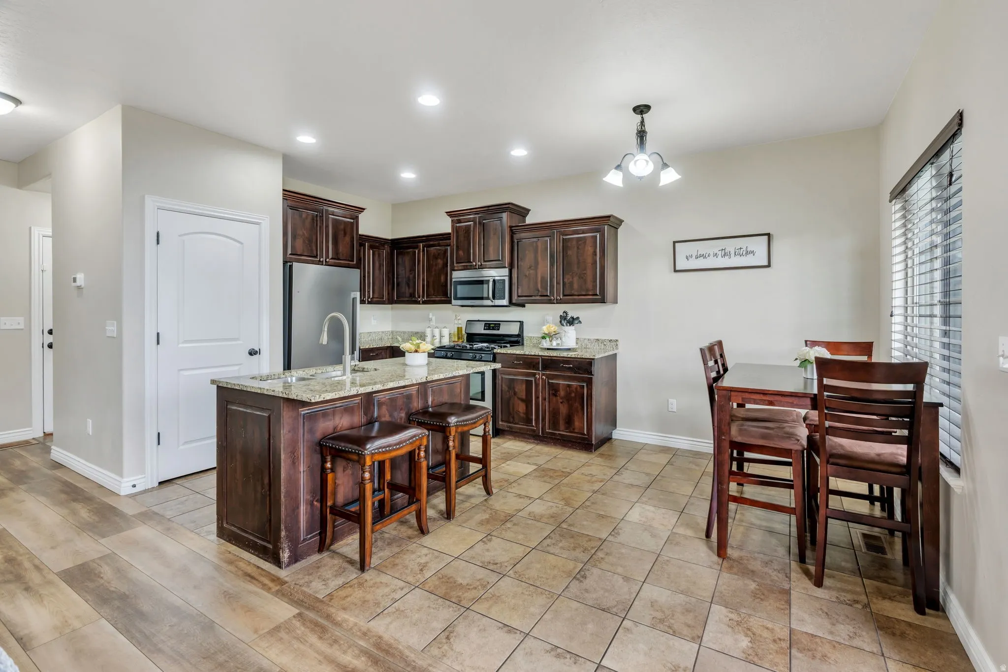 Kitchen featuring an island with granite countertop, stainless steel appliances, dark wood cabinetry, recessed lighting, and tile flooring