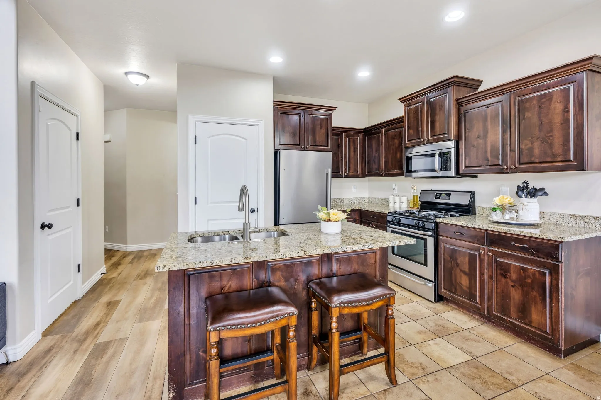 Kitchen featuring dark wood cabinetry, stainless steel appliances, a center island with double sink, granite countertops, and recessed lighting