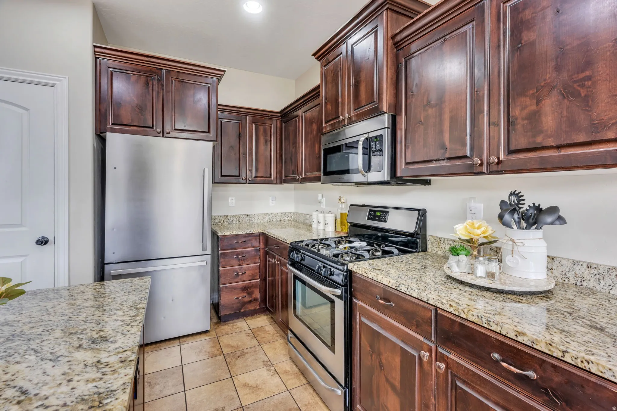 Kitchen featuring rich wood-finish cabinetry, light speckled countertops, stainless steel appliances, and tiled flooring