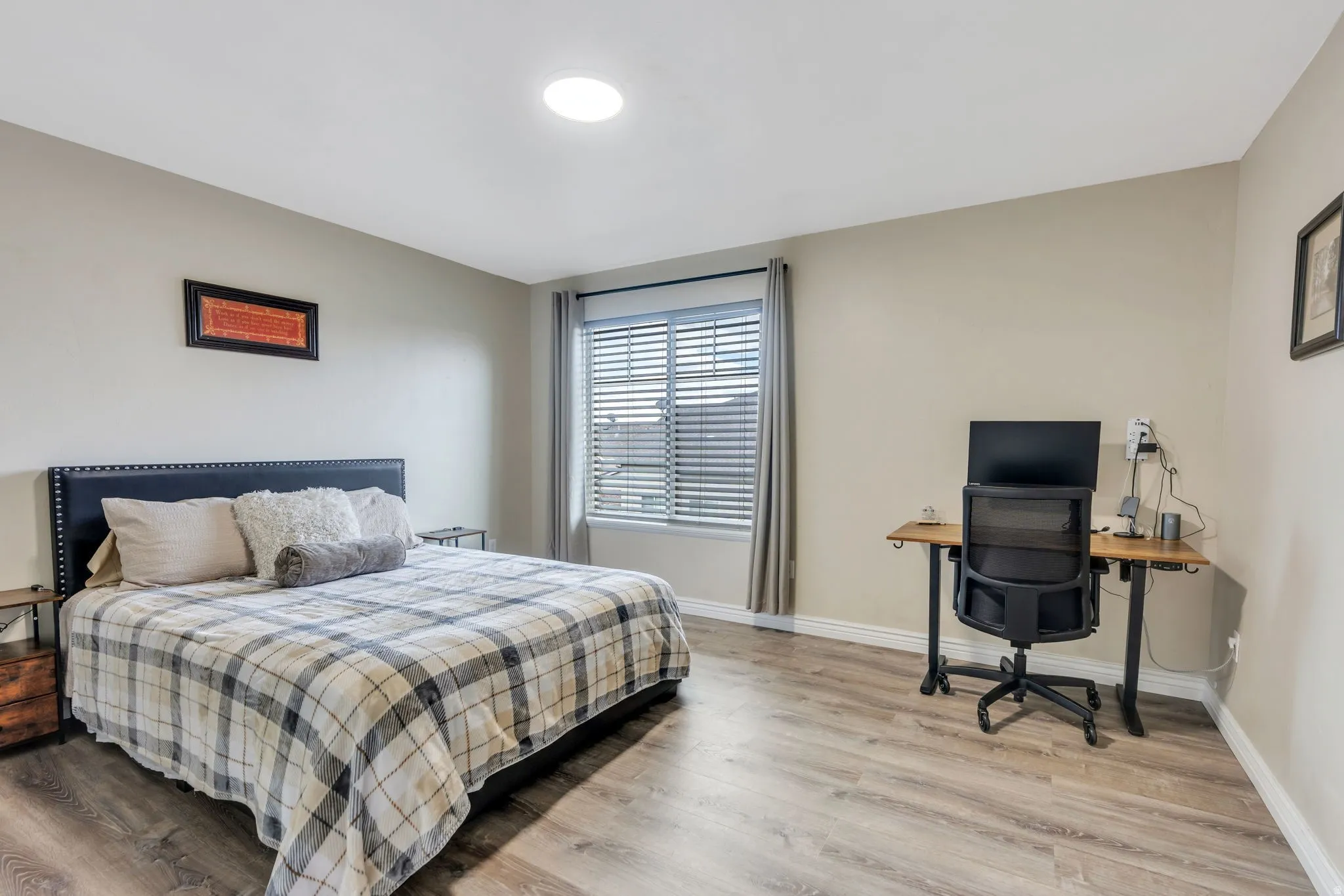 Generously sized room featuring wood-finish flooring, a window with horizontal blinds and drapery, and neutral wall tones
