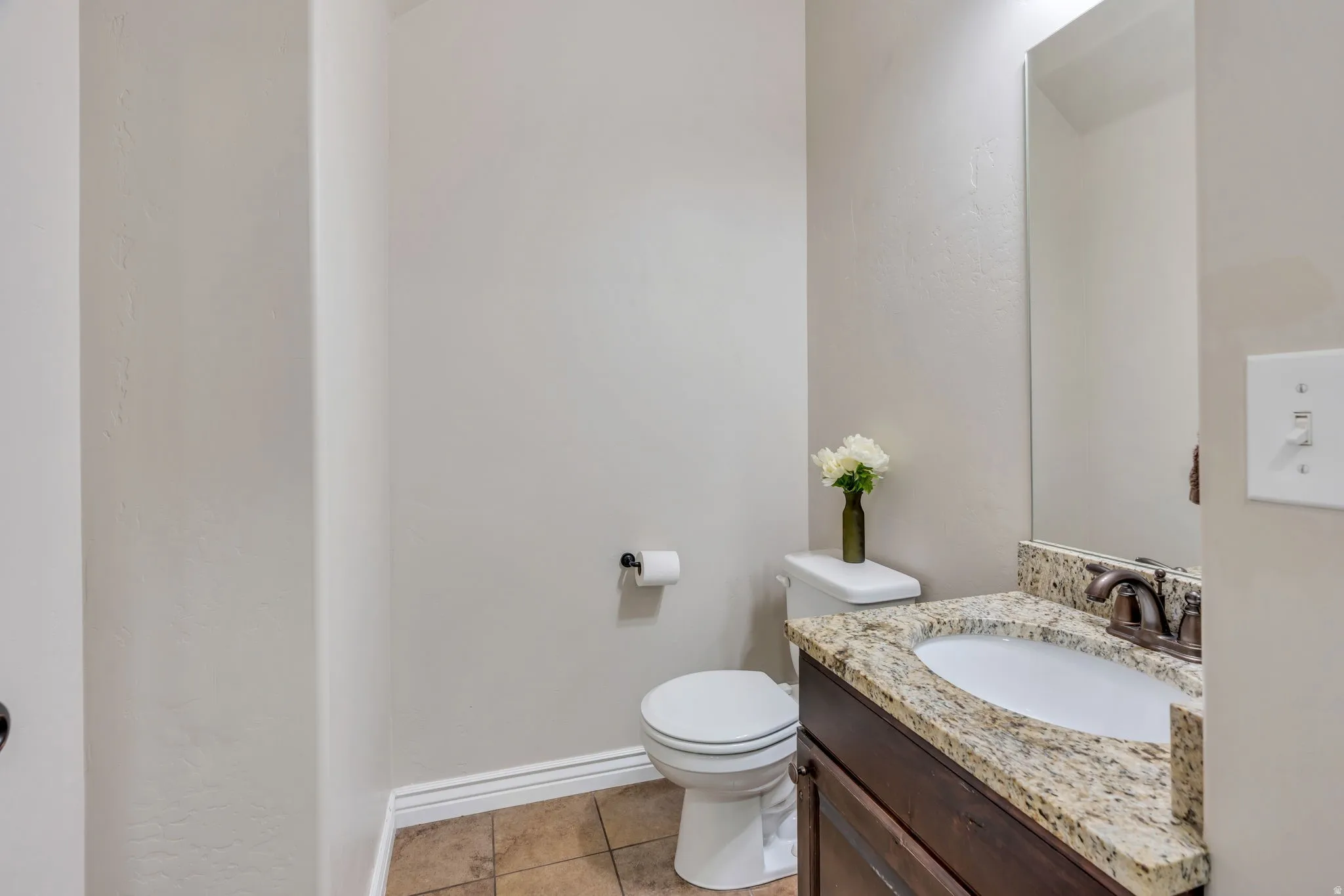 Powder room featuring a brown wood-finish vanity with an undermount sink, a patterned stone countertop, and an oil-rubbed bronze faucet