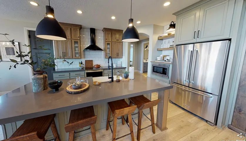 Open-concept kitchen featuring an island with a solid surface countertop, stainless steel appliances, a black range hood, light wood-finish flooring, and pendant lighting