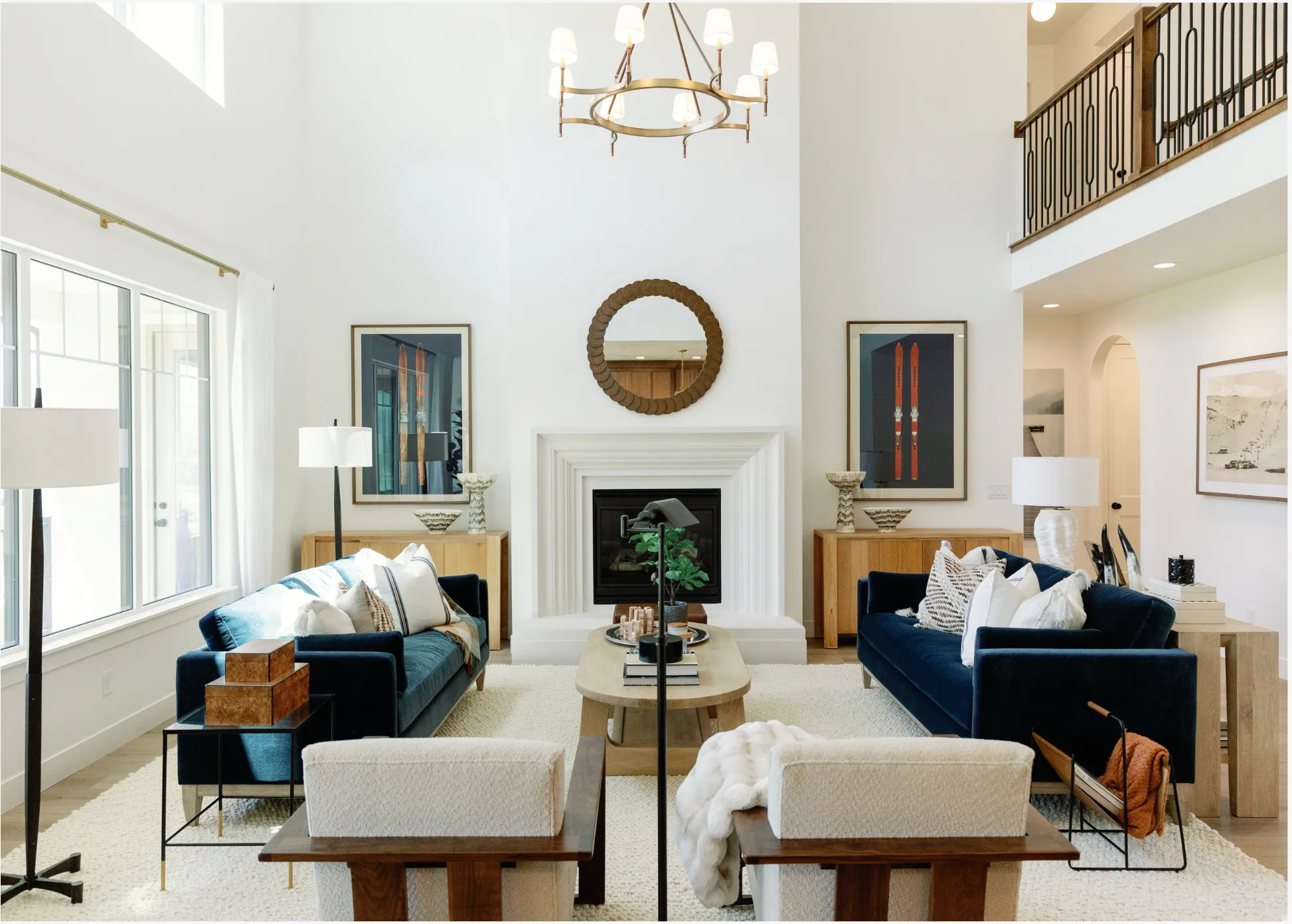 Two-story living area featuring a central fireplace with an ornate mantel, a gold-finish chandelier, and a second-story balcony with decorative metal railings