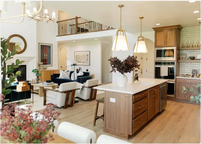 Open-concept living space featuring wood-finish flooring, a kitchen island with integrated sink, stainless steel built-in appliances, and a fireplace with a white mantel