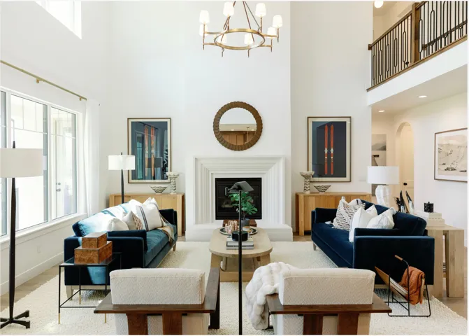 Two-story living area featuring a central fireplace with an ornate mantel, a gold-finish chandelier, and a second-story balcony with decorative metal railings