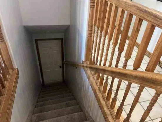 Staircase featuring wood railings and balusters, carpeted treads, and a white door at the bottom