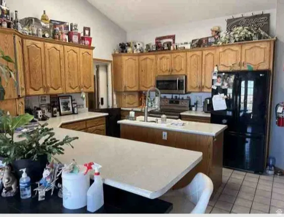 Kitchen featuring extensive wood cabinetry, L-shaped countertop, center island with sink, stainless steel microwave, and black refrigerator