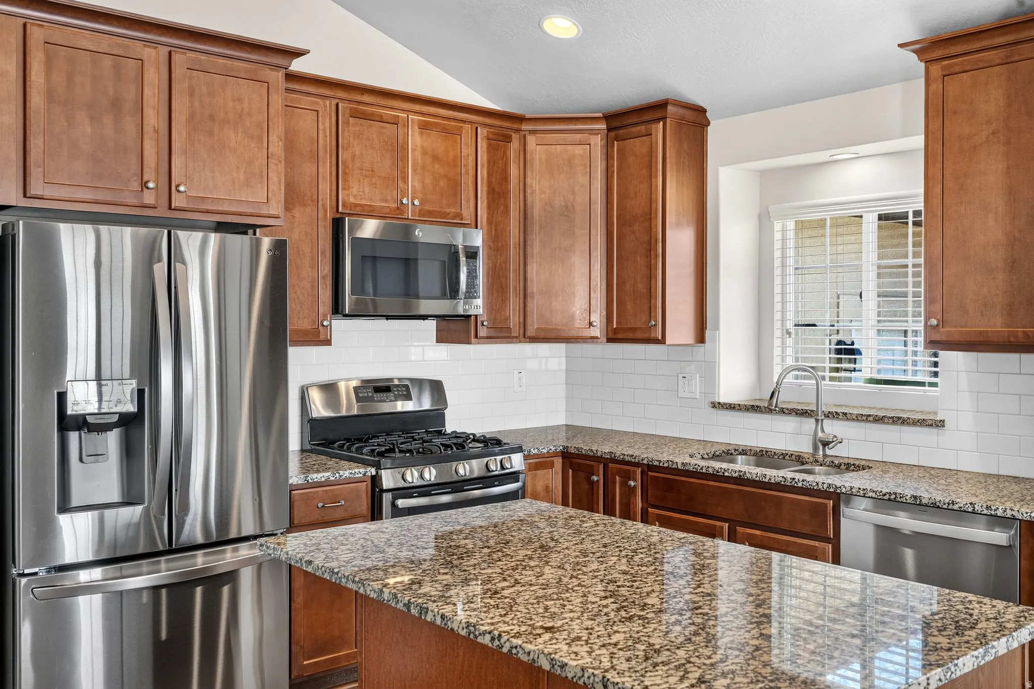 Kitchen with stainless steel appliances, wood-finish cabinetry, granite countertops, an island, and subway tile backsplash