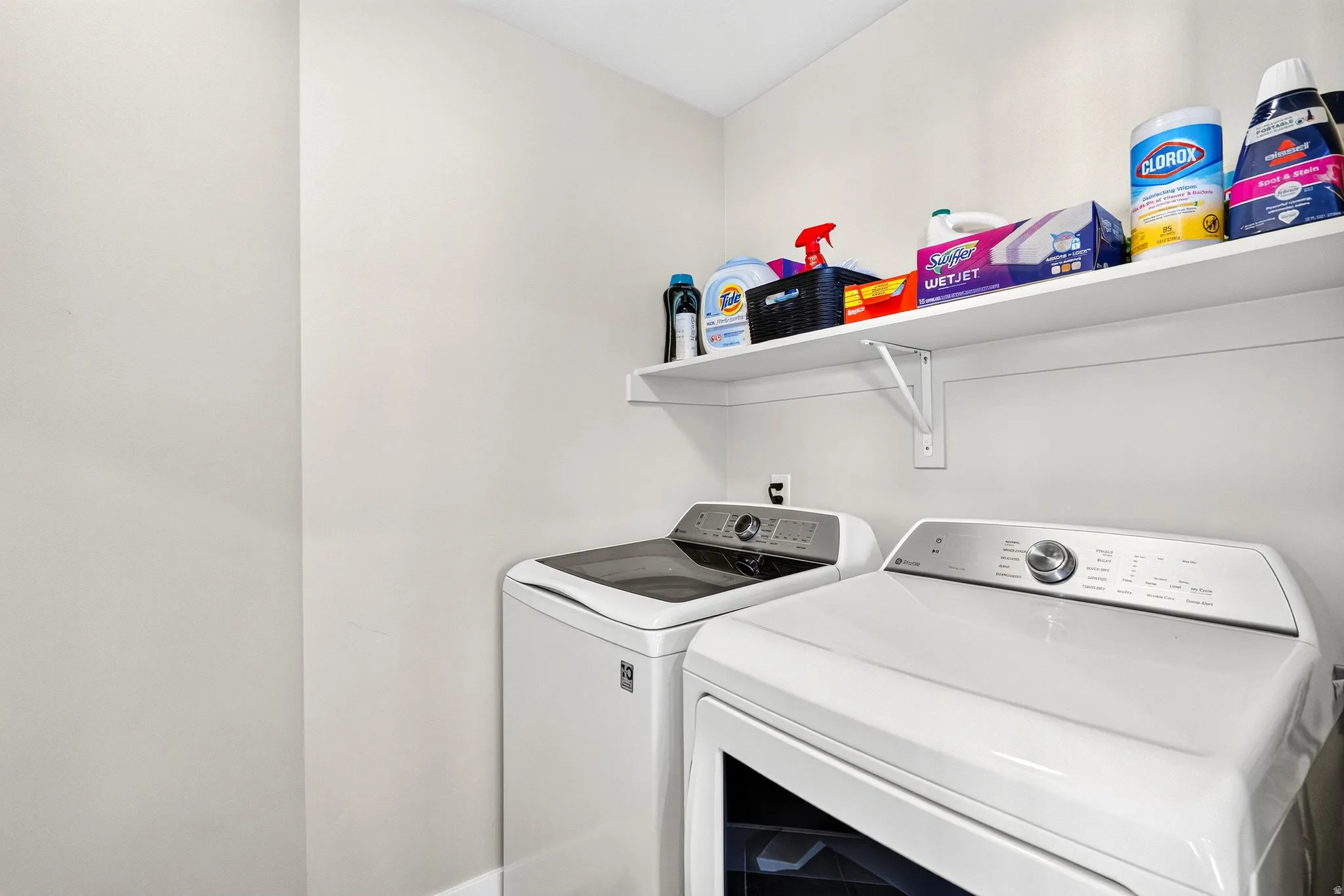 Dedicated laundry area featuring white walls and a white wall-mounted shelf
