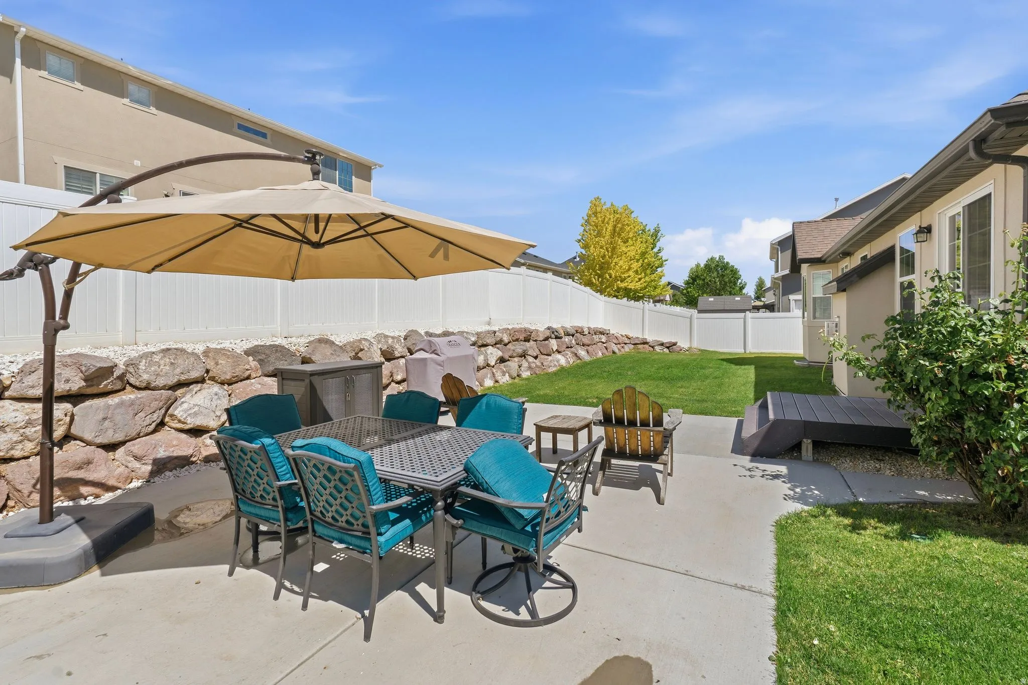 Spacious backyard featuring a concrete patio, a manicured lawn, a retaining wall with natural stone, and privacy fencing