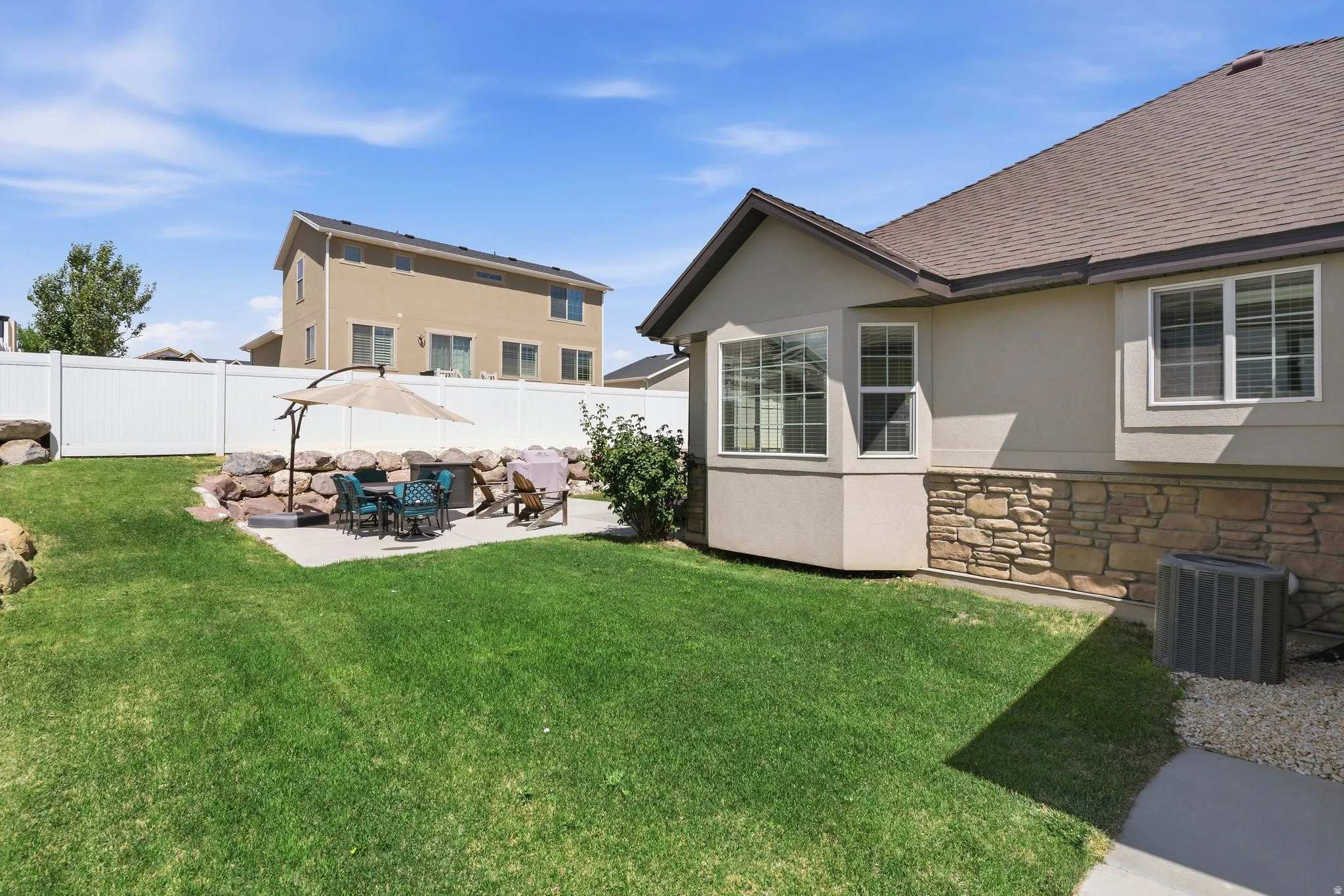 Expansive backyard featuring a concrete patio, a stone retaining wall, and a large lawn area