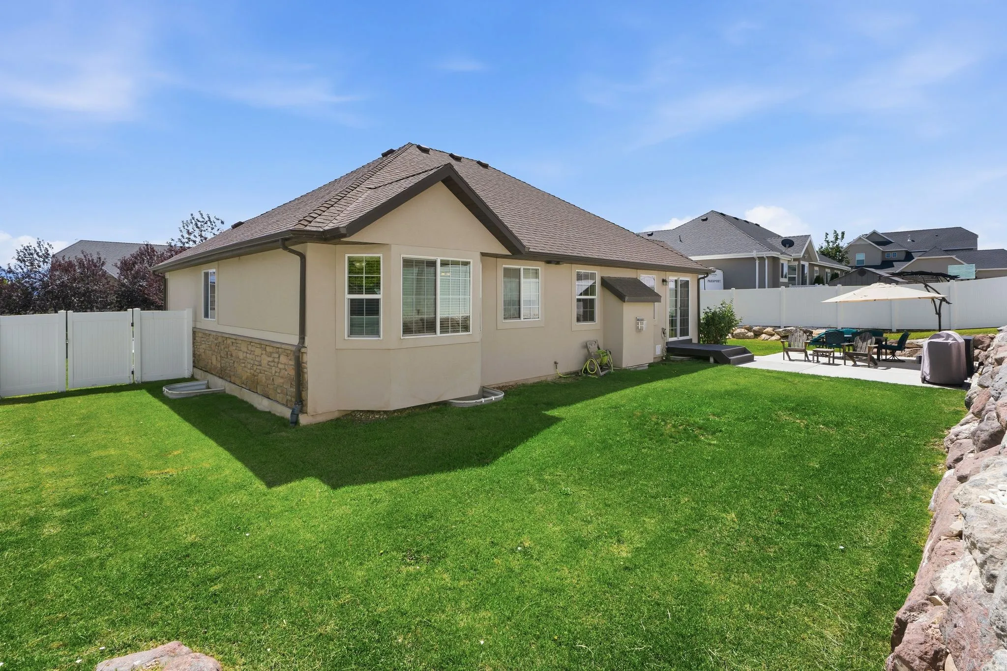 Expansive fenced backyard featuring a manicured lawn, stone veneer siding, and a concrete patio