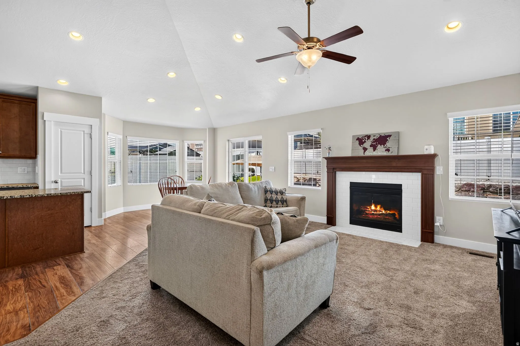 Living room featuring a central fireplace with wood mantel and white tile surround, vaulted ceilings, recessed lighting, and a ceiling fan