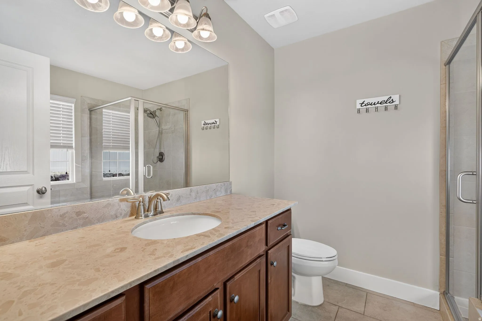 Bathroom featuring a wood-finish vanity with an undermount sink, a light-toned countertop, and a glass-enclosed shower with tiled walls