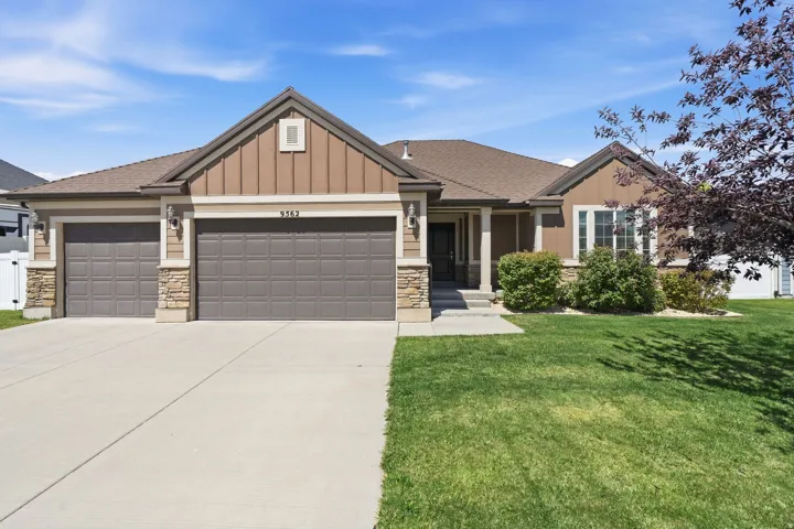Ranch-style residence featuring a two-car garage, stone accents, board-and-batten siding, a covered entry, and a verdant lawn