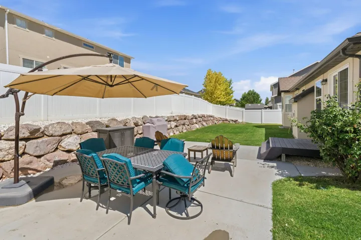 Spacious backyard featuring a concrete patio, a manicured lawn, a retaining wall with natural stone, and privacy fencing