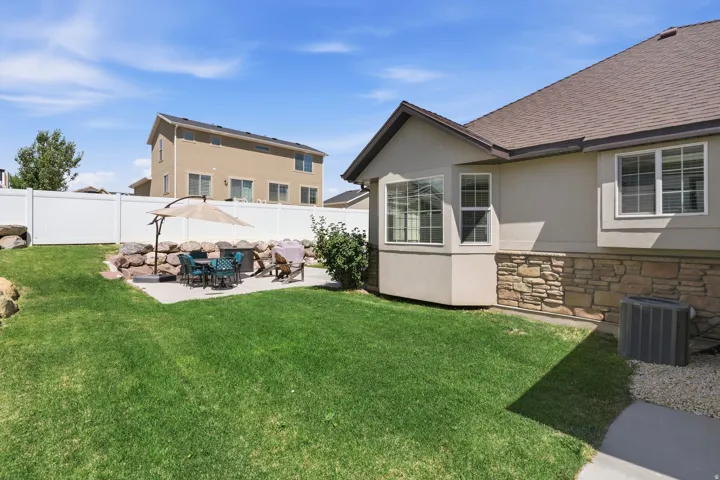 Expansive backyard featuring a concrete patio, a stone retaining wall, and a large lawn area
