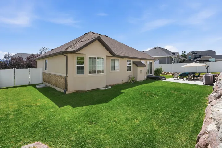 Expansive fenced backyard featuring a manicured lawn, stone veneer siding, and a concrete patio