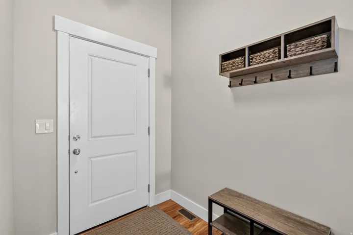 Entryway featuring wood-finish flooring, a white paneled door with polished chrome hardware, light gray wall paint, and a built-in wood-finish storage shelf with integrated hooks