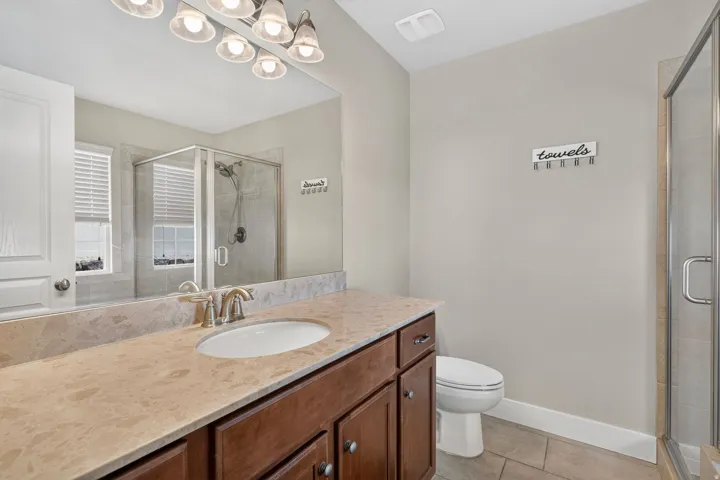 Bathroom featuring a wood-finish vanity with an undermount sink, a light-toned countertop, and a glass-enclosed shower with tiled walls