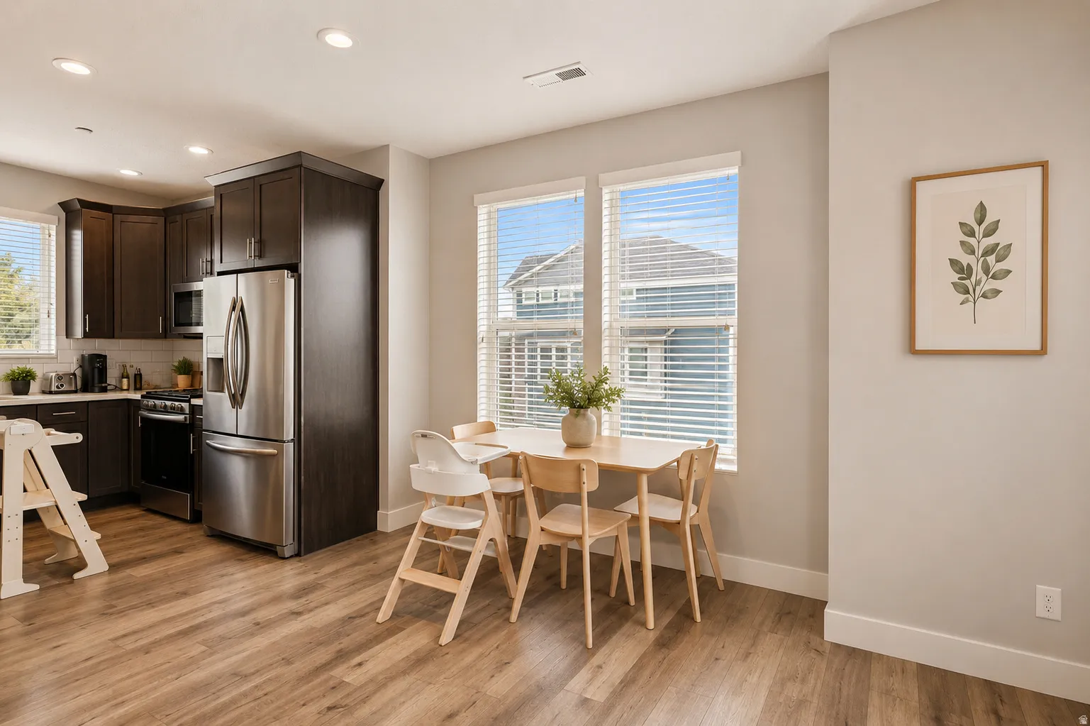 Open-concept kitchen featuring dark wood cabinetry, stainless steel appliances, wood-finish flooring, recessed lighting, and a dining area with twin windows