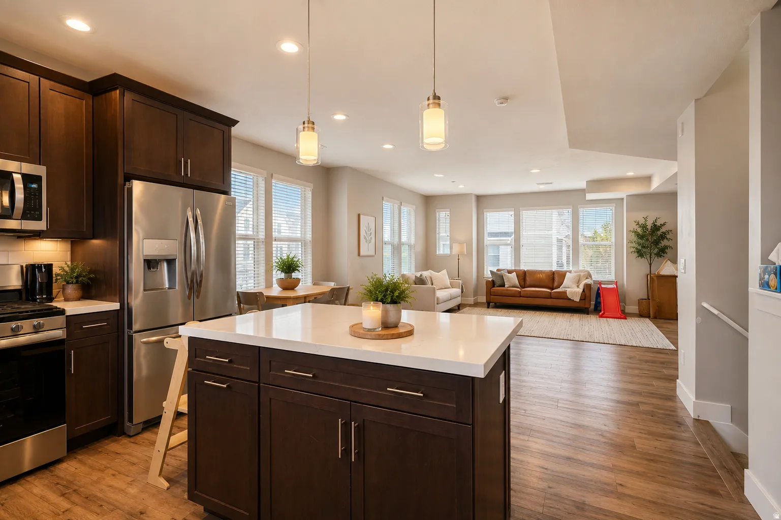 Open-concept living space featuring a kitchen island with a light-toned countertop, dark wood-finish cabinetry, stainless steel appliances, and wood-finish flooring throughout